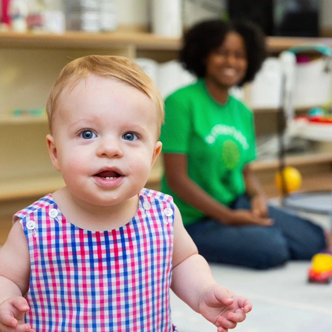 Baby standing with sitter in background